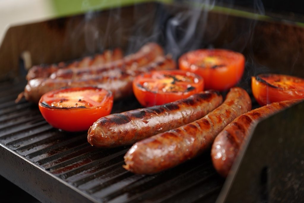 saucisses et tomates en train de cuire sur une plancha à gaz puissante